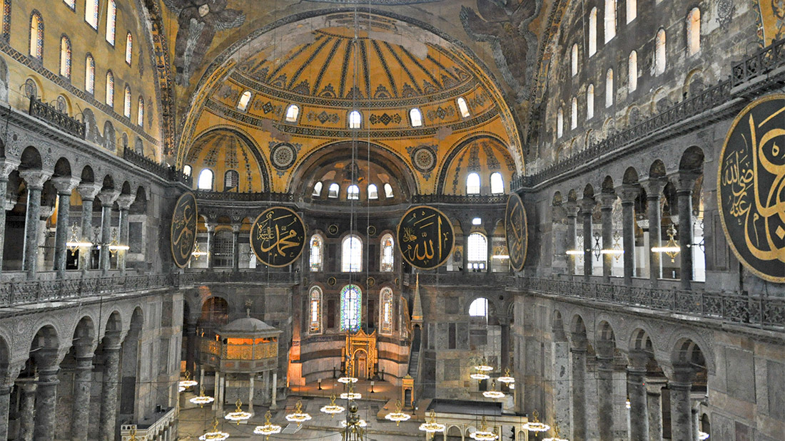 Interior perspective of Hagia Sophia (Ayasofya) taken from the upper gallery, showing the monumental Byzantine dome and Islamic calligraphy.